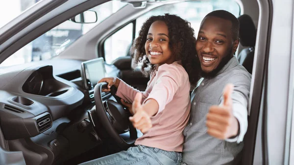 Feliz padre negro y la hija sentados en el asiento del conductor del coche nuevo, mostrando el pulgar hacia arriba, recomendando concesionario de automóviles — Foto de Stock