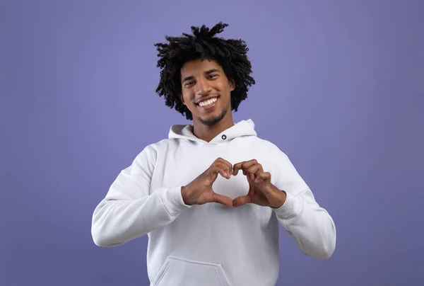 Tipo adolescente negro moldando as mãos como o coração perto de seu peito, fazendo gesto de amor no fundo do estúdio violeta — Fotografia de Stock