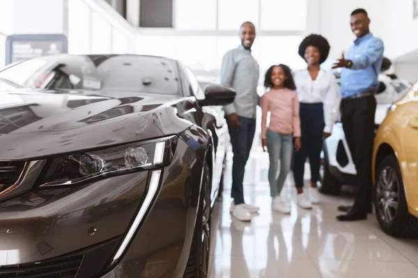 Jovem vendedor feliz ajudando a família afro-americana escolher carro de luxo na concessionária de veículos, foco seletivo — Fotografia de Stock