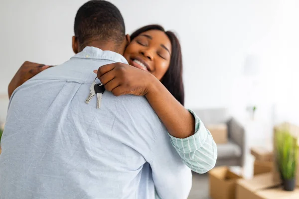 Happy black lady with keychain hugging her husband and smiling, celebrating moving to their house, free space — Stock Photo, Image