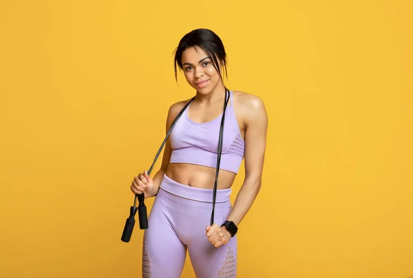 Conceito de estilo de vida ativo. Mulher negra magro segurando pulando corda posando e sorrindo para a câmera sobre fundo amarelo — Fotografia de Stock