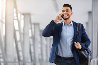 Havaalanında yürürken cep telefonuyla konuşan gülümseyen Orta Doğulu adam.