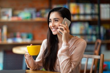 Kahvede tek başına dinlenirken cep telefonuyla konuşan gülümseyen Latin bayan, yan bakıp gülümsüyor, boşluğu kopyalıyor.