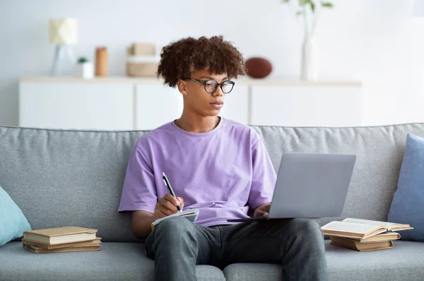 Sério adolescente afro-americano tendo aula on-line sobre laptop, tomando notas durante palestra na web em casa — Fotografia de Stock
