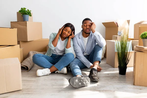 Portret van vermoeide Afro-Amerikaanse echtgenoten uitgeput na verhuizing naar nieuw appartement, zittend tussen kartonnen dozen — Stockfoto