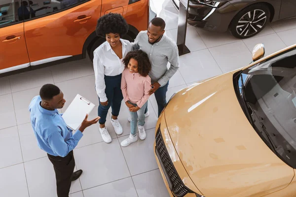 Milenyum siyahi ailesinin yeni araba alması ya da kiralamasının ötesinde, oto galerisinde danışman bir satıcı — Stok fotoğraf