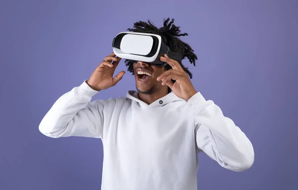 Funky Afro nastolatek noszący słuchawki VR, odkrywający cyberprzestrzeń, wykorzystujący wirtualną rzeczywistość do rozrywki na fioletowym tle — Zdjęcie stockowe