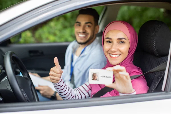 Gelukkig moslim vrouw zitten in auto met instructeur en tonen rijbewijs — Stockfoto