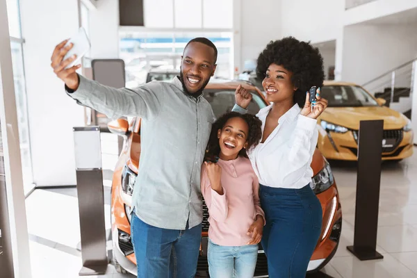 Família negra excitada levando selfie com chave de carro depois de comprar novo veículo na concessionária de automóveis — Fotografia de Stock