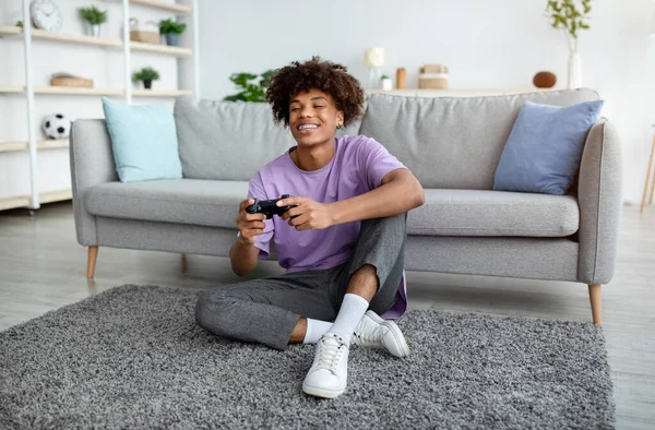 Full length of positive black teen gamer with controller playing online video games, sitting on floor at home — Stock Photo, Image