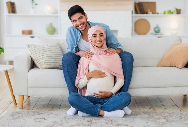 Massage tijdens de zwangerschap concept. Jonge Arabier man masseert zijn vrouw schouders, rust samen thuis — Stockfoto