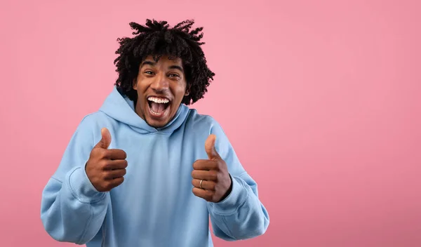 Retrato de chico adolescente afroamericano funky mostrando pulgares hacia arriba gesto sobre fondo rosa, pancarta con espacio libre —  Fotos de Stock