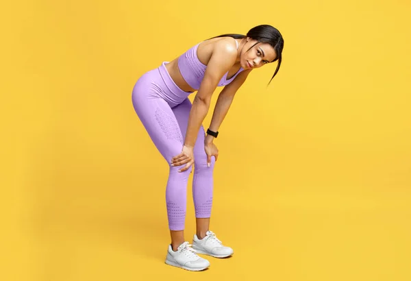 Fáradt afro-amerikai hölgy figyelembe szünet edzés, pihenés, támaszkodó térdre sárga stúdió háttér — Stock Fotó
