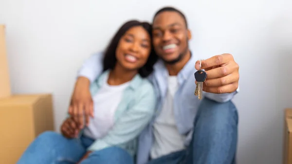 Novo lar. Esposos negros excitados mostrando chaves, sentados em sua própria casa após a realocação, foco na chave, panorama — Fotografia de Stock