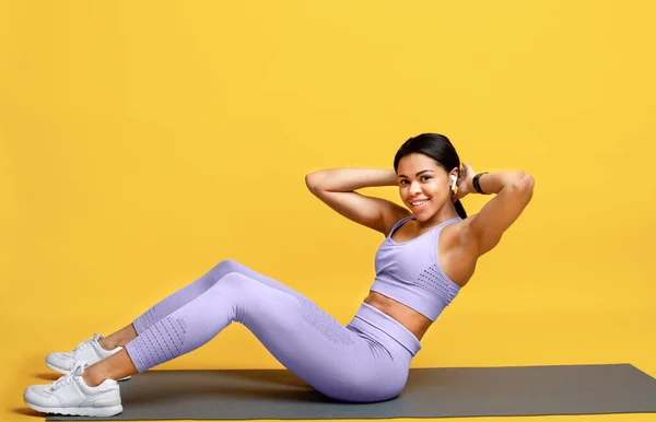 Millennial Afrikaans amerikaanse vrouw doen buikspieren oefeningen op sport mat over geel studio achtergrond — Stockfoto