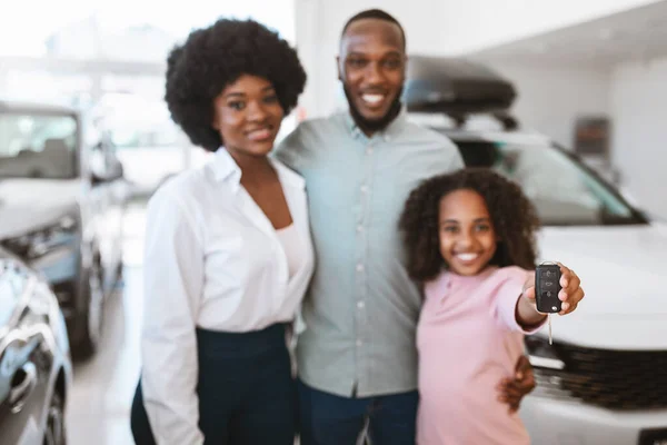 Menina preta bonito mostrando chave do carro, de pé com seus pais na concessionária de automóveis, foco seletivo. Espaço de cópia — Fotografia de Stock