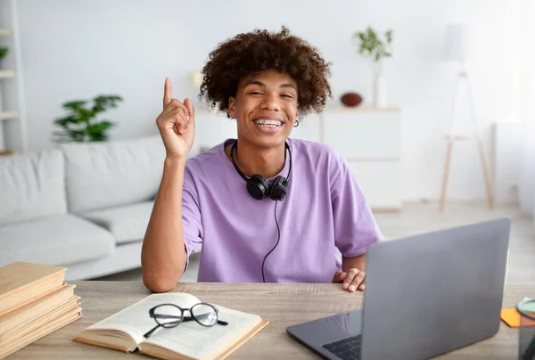 Estudante adolescente preto feliz com fones de ouvido com ideia criativa perto do laptop, gesto eureka em casa — Fotografia de Stock