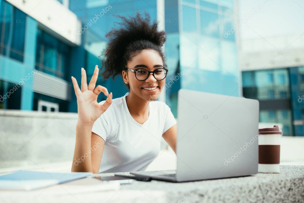 African American Female Student Gesturing Okay Using Laptop Sitting Outside