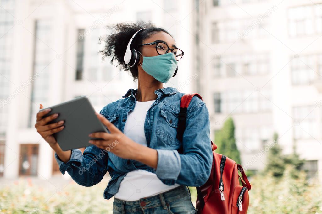Black Student Girl Using Tablet Wearing Headphones And Mask Outdoors