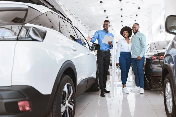 Otomobil galerisindeki arkadaş canlısı satıcıyla konuşarak yeni araba alan mutlu genç siyah çift. — Stok fotoğraf
