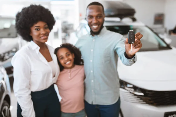 Vidám fekete fickó feleségével és lányával, autókulcsot mutat, boldog új jármű vásárlása felett az autókereskedésben — Stock Fotó