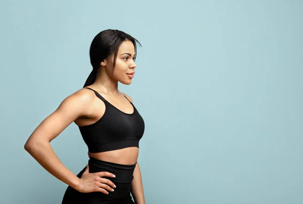 Un personal trainer. Fiducioso nero sport donna posa su sfondo blu studio e guardando lo spazio libero — Foto Stock
