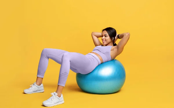 Deportiva mujer negra haciendo ejercicios abdominales en la pelota de fitness sobre fondo de estudio amarillo, espacio libre —  Fotos de Stock