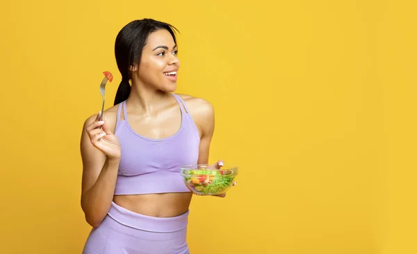 Nutrição saudável. Apto senhora preta comer salada de legumes e olhando para o espaço livre, de pé sobre fundo amarelo — Fotografia de Stock