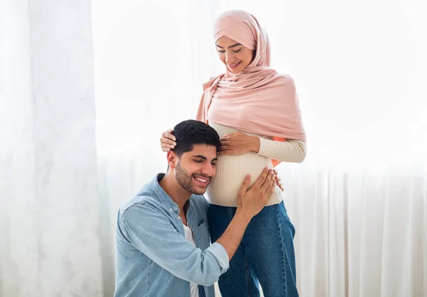 Gelukkige Arabier man drukt zijn oor tegen zijn vrouw zwangere buik, luisteren naar zijn baby 's hartslag, vrije ruimte — Stockfoto
