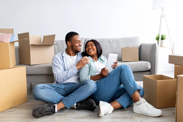 Liefdevolle zwarte familie met behulp van digitale tablet en omarmen terwijl zitten op de vloer in nieuw huis tussen uitgepakte dozen — Stockfoto