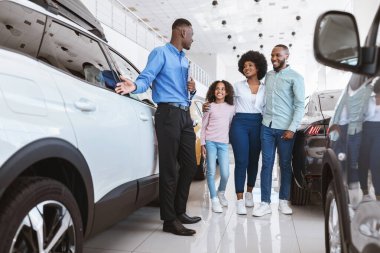 Genç siyahi aile otomobil galerisinden yeni araba almak için kendinden emin satış temsilcisiyle konuşuyor.