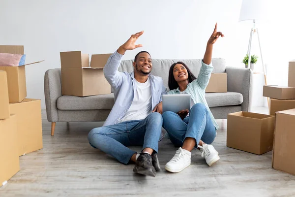 Africano casal americano discutindo design de novo apartamento, sentado no chão e usando tablet digital, planejamento de renovação — Fotografia de Stock