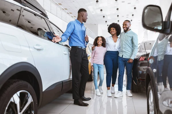 Jovem família negra tendo conversa com agente de vendas confiante sobre a compra de carro novo na concessionária de automóveis — Fotografia de Stock