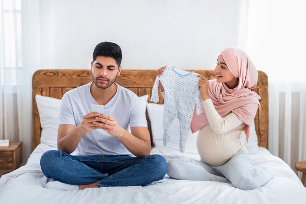 Concetto di dipendenza da gadget. Careless marito musulmano utilizzando smartphone, ignorando la moglie incinta — Foto Stock
