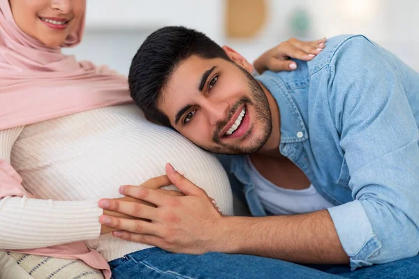 Futuro padre. Emocionado hombre musulmán escuchando a sus esposas embarazadas vientre, amante árabe chico abrazando gran barriga, primer plano — Foto de Stock