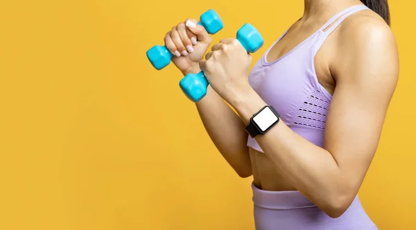 Unrecognizable african american lady exercising with two blue dumbbells, wearing fitness tracker with blank screen