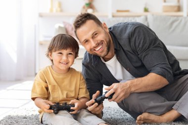 Mutlu bir baba oğluyla hafta sonunun tadını çıkarıyor. Oyun çubuklarıyla oyun oynuyor, kameraya gülümsüyor.