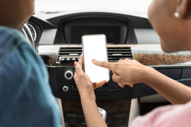 Siyah adam ve kadın arabada cep telefonu kullanıyor.