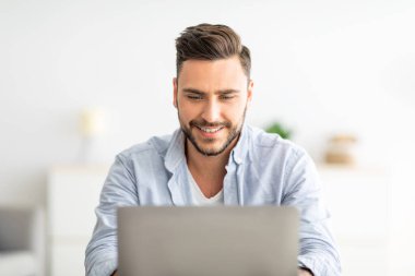 Merkez ofis konsepti. Bilgisayarda çalışan mutlu adamın yakın plan portresi. Ev içi işyerinde oturuyor.