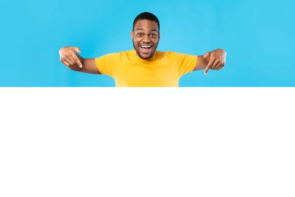Izgalmas fekete ember mutató üres fehér tábla, kék háttér — Stock Fotó