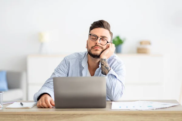 Overworked young freelancer man sitting at workplace and sleeping, napping while working on laptop, copy space — Stock Photo, Image