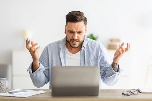 Uomo arrabbiato millenario guardando lo schermo del computer portatile e gesticolando, avendo software, errore del sito web, seduto all'interno di casa — Foto Stock