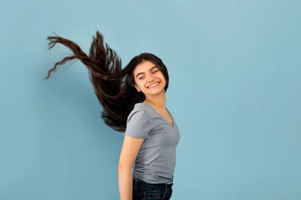 Retrato de sorridente adolescente indiana posando com longos cabelos escuros voando no fundo do estúdio azul — Fotografia de Stock