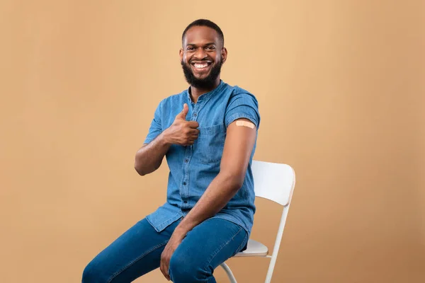 Homem negro com ajuda de banda no braço recomendando vacinação anti-vívida, mostrando o polegar para cima, recebendo vacina contra o coronavírus — Fotografia de Stock