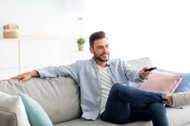 Boş zaman ve eğlence. Mutlu adam televizyon seyrediyor uzaktan kumandayla televizyon kanallarını değiştiriyor, kanepede oturuyor.