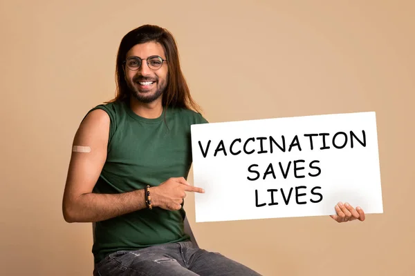 Sonriente chico de oriente medio apuntando a bordo de la vacuna salva vidas — Foto de Stock