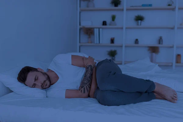 Beteg Y-generációs férfi szenved gyomorfájás, ölelkező gyomor, miközben fekszik az ágyban éjszaka, másolja tér — Stock Fotó