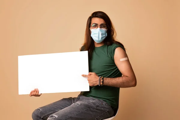 Middle-eastern vaccinated man in face mask with empty board — Stock Photo, Image