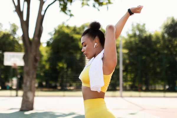 Deportiva mujer negra en ropa deportiva amarilla que se extiende escuchando música — Foto de Stock