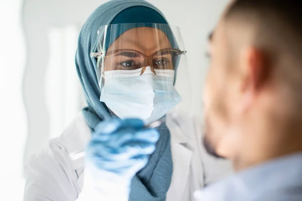 Dentista islámica en Hijab y escudo facial examinando los dientes de los pacientes masculinos —  Fotos de Stock